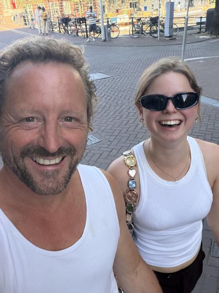 A cheerful selfie captures two people, a man and a woman, smiling broadly on a sunny day in Amsterdam